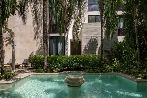 Courtyard pool with a stone fountain, surrounded by palm trees and a modern stone building