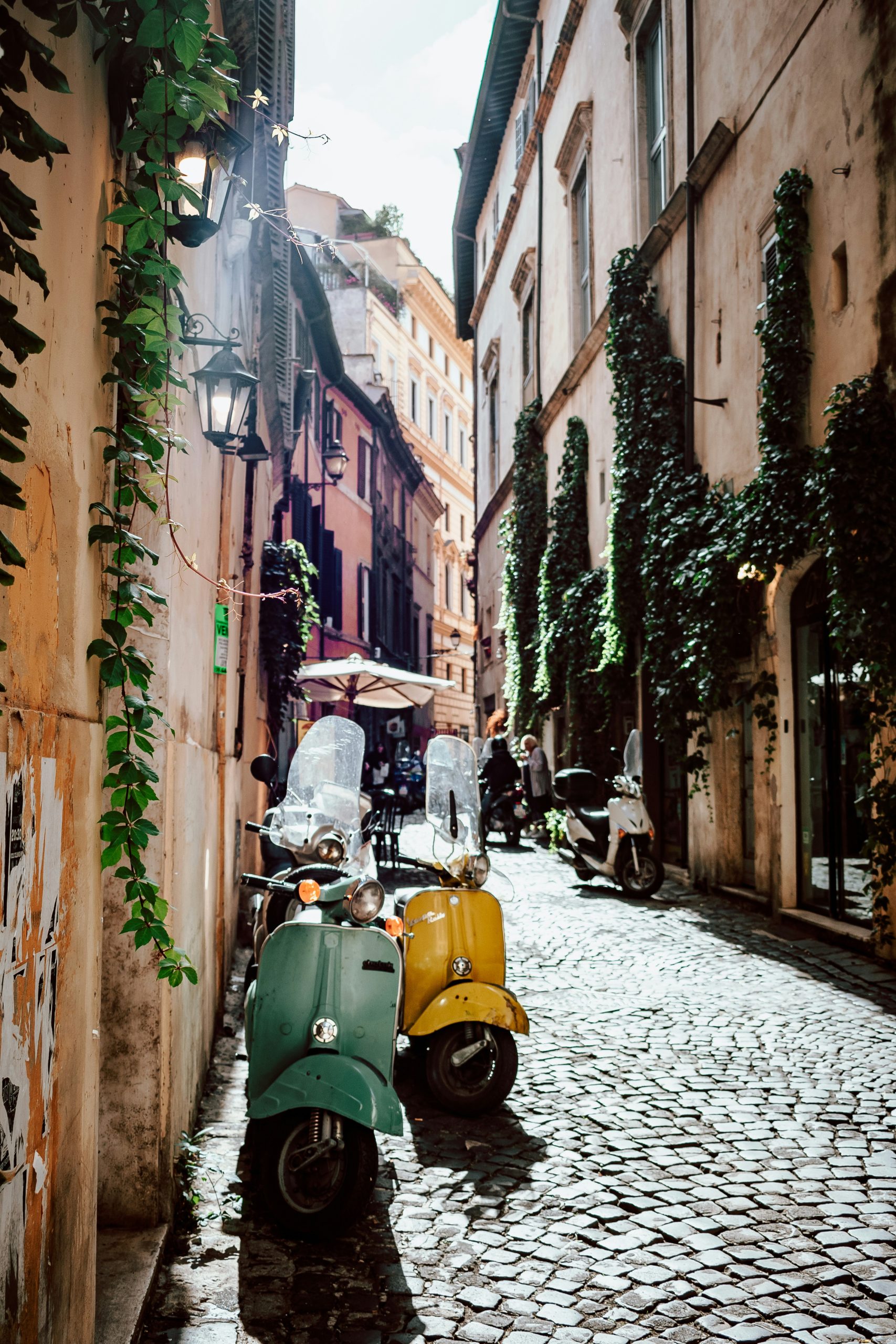 Cobblestone alley in Rome with ivy-covered walls and two parked vintage scooters
