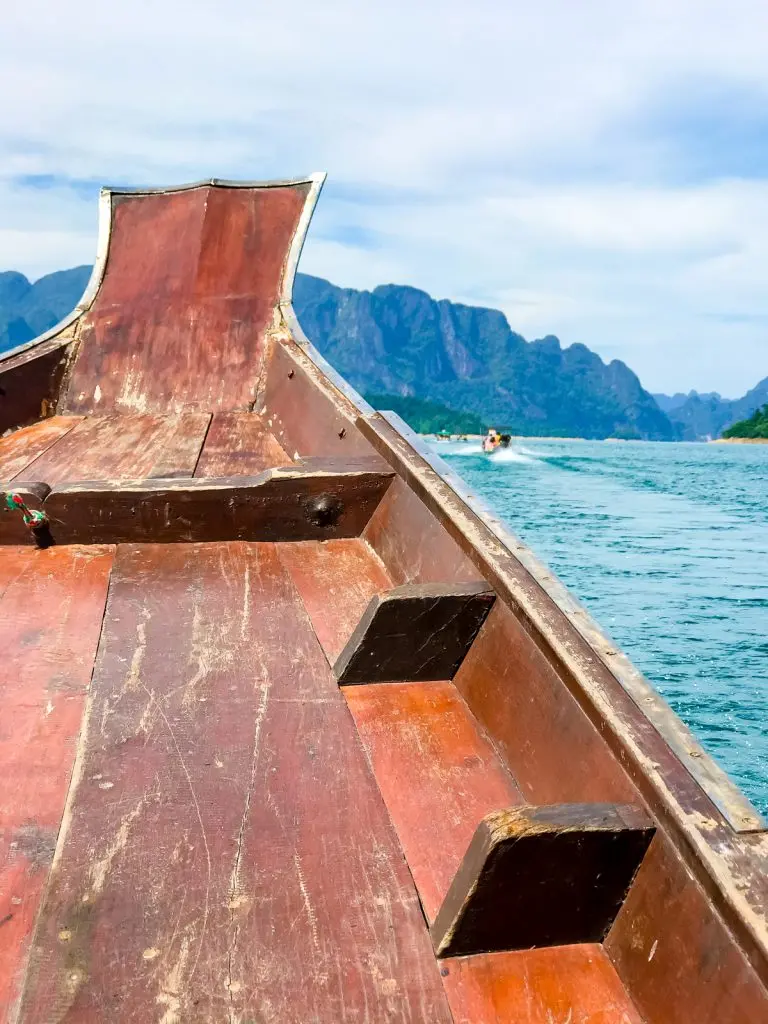 View from the bow of a wooden longtail boat on blue water with limestone hills ahead